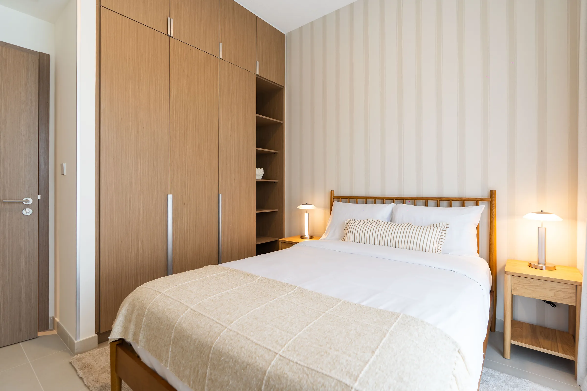 Furnished bedroom with timber wardrobes, bedside lamps and striped cushions
