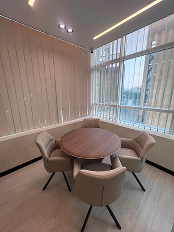 Small meeting room with round timber table, four chairs and vertical blinds
