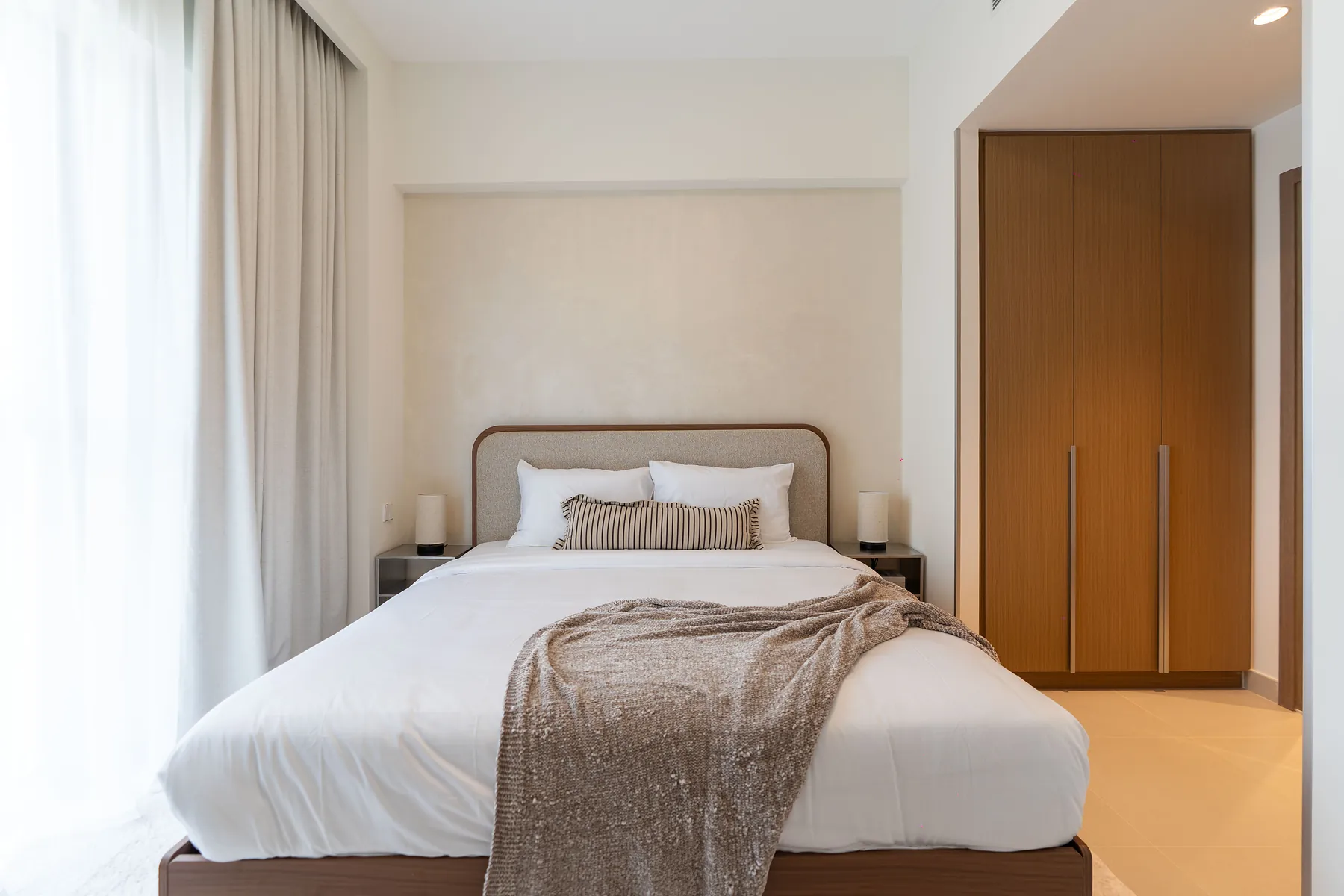Bedroom with curved upholstered headboard, timber wardrobe and sheer curtains