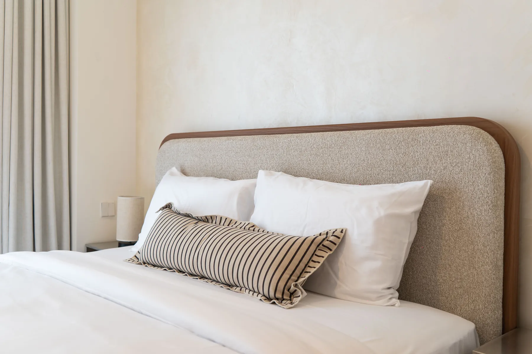 Curved upholstered headboard with white pillows and striped cushion