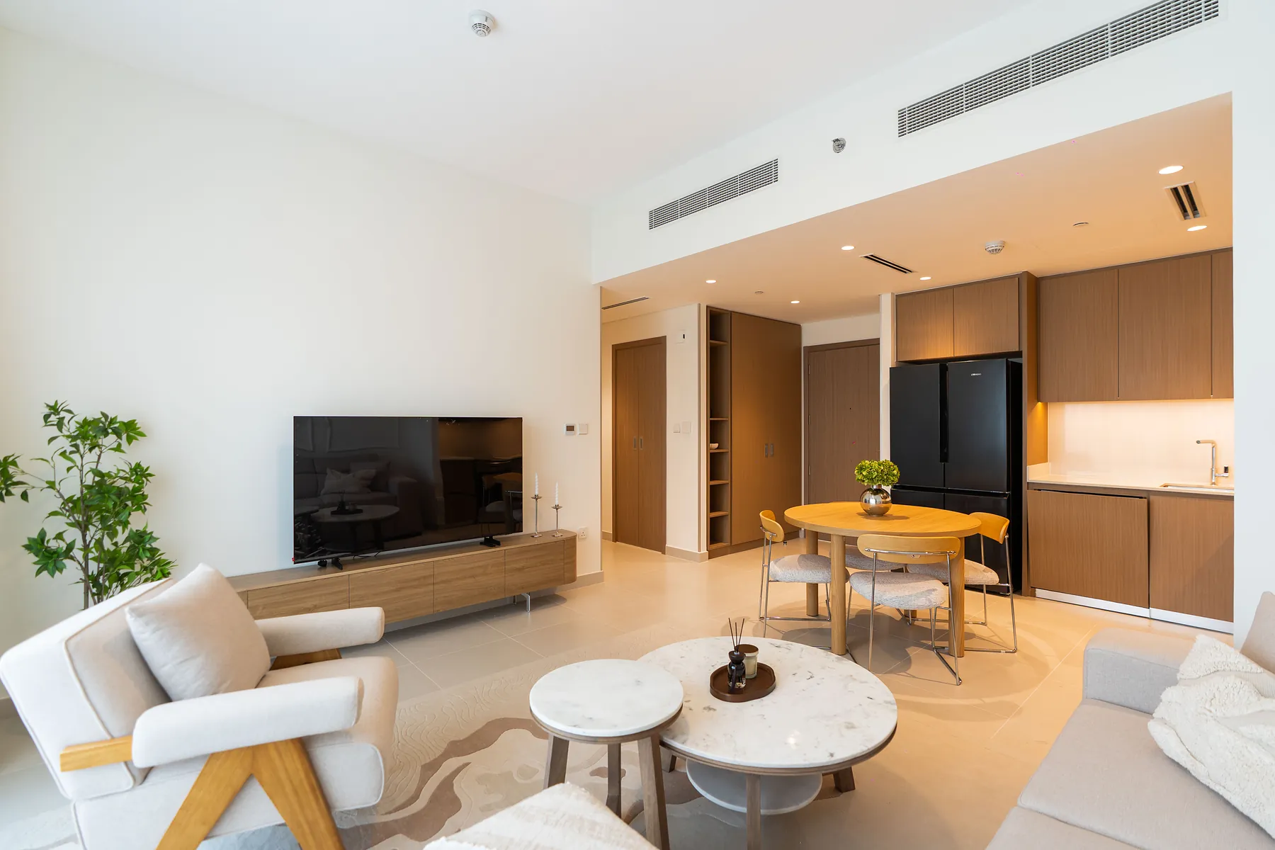 Living area with a timber TV unit, lounge chair, marble coffee tables and open kitchen behind